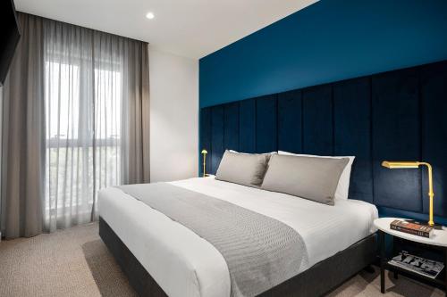 a bedroom with a large bed with a blue wall at Quest Burwood East in Burwood