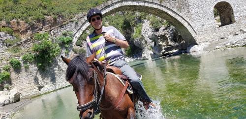 a man riding a horse in the water near a bridge at Funky Guest House & Adventures in Përmet