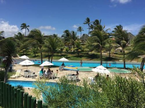 a resort swimming pool with people sitting on chairs and umbrellas at Beach Class Resort 2 quartos Muro Alto BMS in Porto De Galinhas