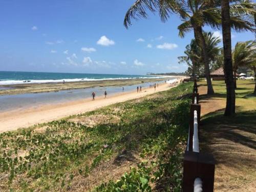 a beach with palm trees and people walking on it at Beach Class Resort 2 quartos Muro Alto BMS in Porto De Galinhas