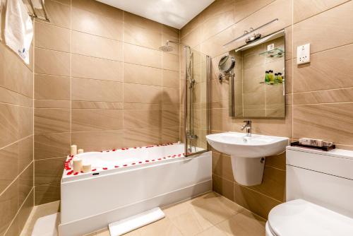 a bathroom with a sink and a tub and a toilet at Grand Sapphire Hotel & Banqueting in Croydon