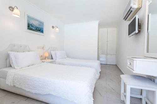 a white bedroom with two beds and a tv at Club Çapa Hotel in Kas