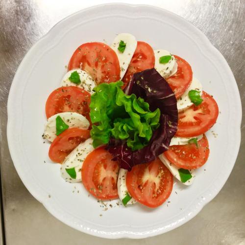 a white plate with tomatoes and greens on it at Villa Belvedere Hotel in Limone sul Garda