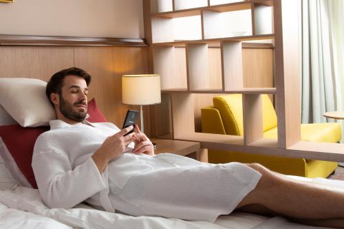 a man laying in bed holding a cell phone at Hotel Premier Aqua - Adults Only in Vrdnik