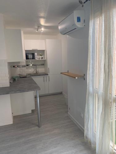 une cuisine avec des armoires blanches, une table et une fenêtre dans l'établissement studio4 27m2 Terrasse Parking Piscine, à Saint-Laurent-du-Var