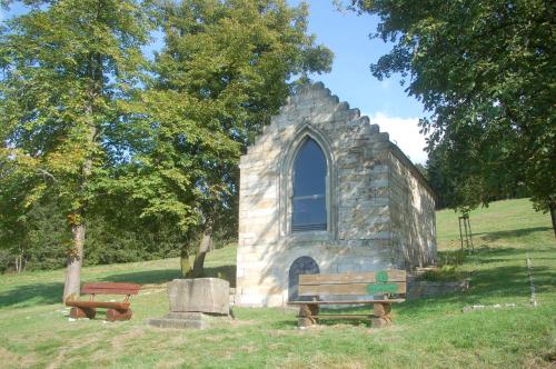a small stone church with two benches in a field at Ferienhaus Waldblick in Siegmundsburg