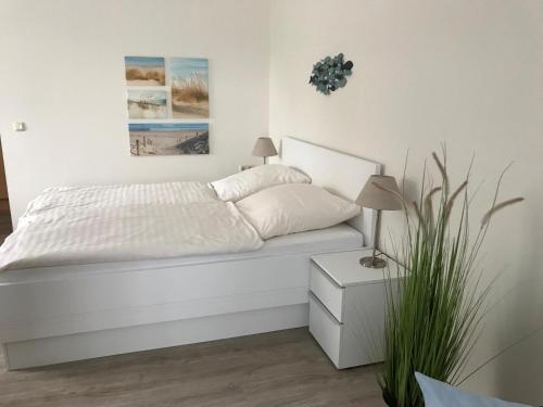 シュタインにあるSteiner Strandappartements Appartement 110 Südseite mit seitlichem Meerblickの白いベッドルーム(植物付)の白いベッド1台