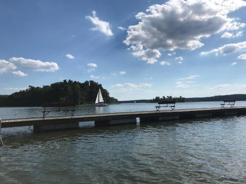 two benches on a dock in the water with a sailboat at Przytulisko na Mazurach in Ruciane-Nida