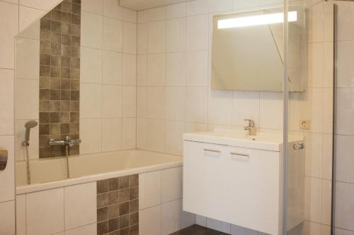 ein Badezimmer mit einem Waschbecken, einer Badewanne und einem Spiegel in der Unterkunft Apartement De Vosseburch in Langeraar