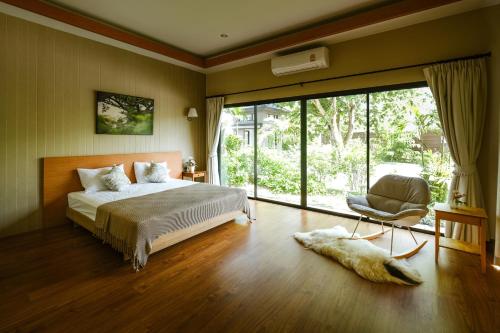 a bedroom with a bed and a chair and a window at At Green Gallery in Si Racha