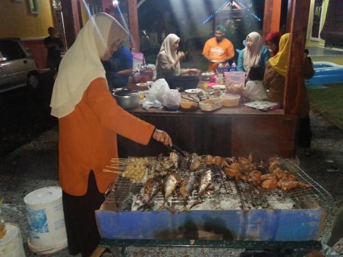 a woman is cooking chickens on a grill at Challet Chengal in Kota Bharu