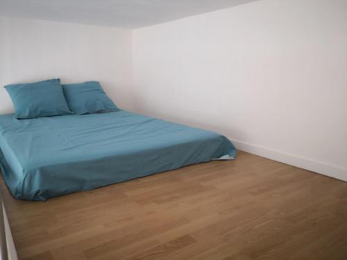 a bed with blue sheets and a wooden floor at studio en plein centre ville à 8 minutes de l'océan in Le Porge
