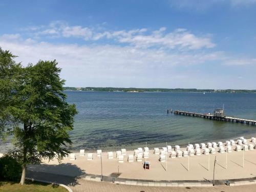 eine Gruppe von Stühlen am Strand mit einem Pier in der Unterkunft Appartement FördeMeer in Glücksburg