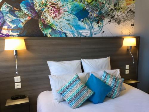 um quarto com uma cama com almofadas e um quadro em Hôtel de L'Avenue em Tarbes