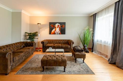 a living room with brown leather furniture and a cow painting on the wall at Lehrerwohnung in Tümlauer Koog