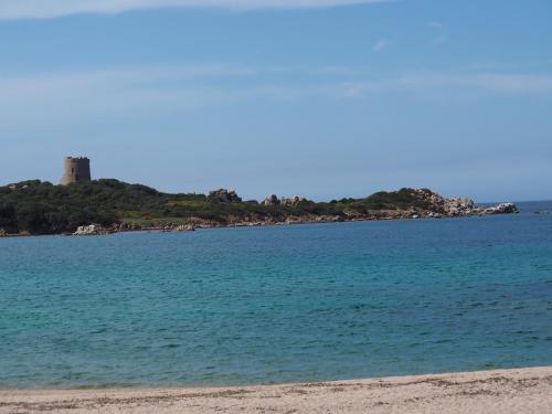 a view of the beach with a lighthouse in the distance at Stazzu Giasti Agriturismo in Aglientu
