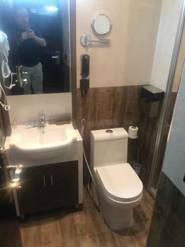 a man taking a picture of a bathroom with a toilet and sink at Castle Hotel in Al Başrah