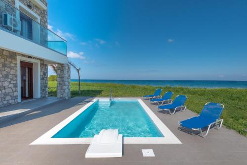 a swimming pool with chairs and the ocean in the background at Diagoras & Attalos Villas in Phanaes