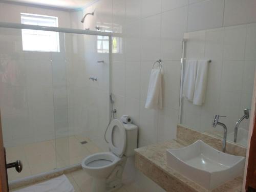 a white bathroom with a toilet and a sink at Hotel Guararapes in Miguel Pereira