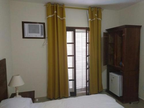 a bedroom with a bed and yellow curtains and a window at Hotel Guararapes in Miguel Pereira