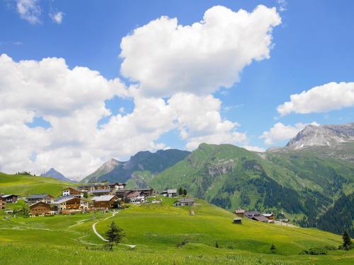 a village on a green hill with mountains in the background at Hotel Mohnenfluh in Lech am Arlberg