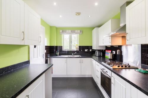 a kitchen with white cabinets and green walls at Riverside cottage in Evesham