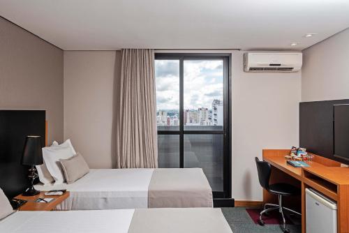 a hotel room with a bed and a desk and a window at Slaviero Curitiba Batel in Curitiba