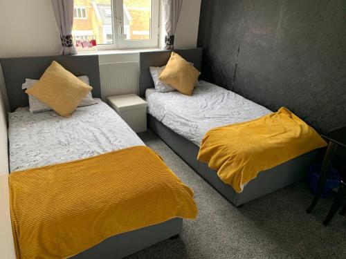 2 camas en un dormitorio con mantas y almohadas amarillas en London budget Maisonette, en Londres