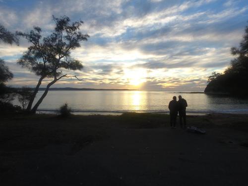 Tres personas de pie en la playa viendo la puesta de sol en Pleasurelea Tourist Resort & Caravan Park, en Batemans Bay