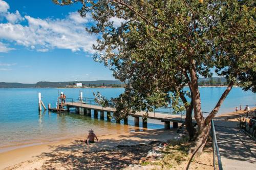 a person sitting on the beach next to a pier at Ettalong Beach Luxury Apartments in Ettalong Beach