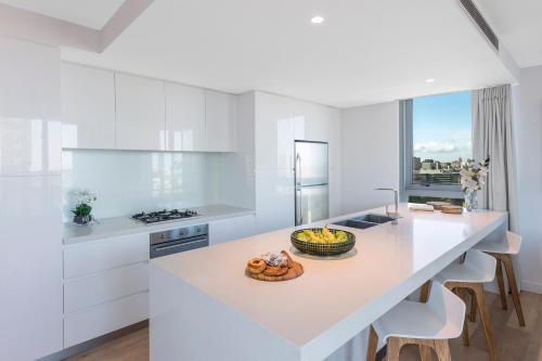 a white kitchen with a white island with a bowl of fruit on it at Imagine Marco in Melbourne