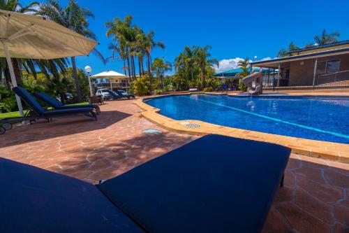 a swimming pool with two chairs and an umbrella at Mountain View Resort in Shoalhaven Heads