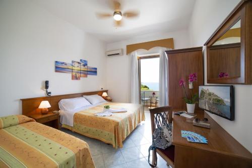 Cette chambre comprend deux lits, une table et un bureau. dans l'établissement Hotel La Mandorla, à Ischia