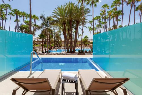 a swimming pool with two tables and chairs next to a swimming pool at Hotel Riu Palace Oasis in Maspalomas