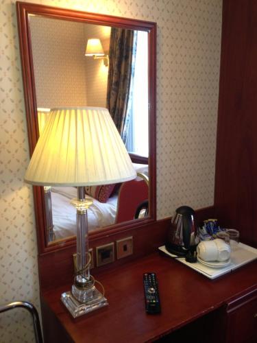 a lamp on a desk in a hotel room with a mirror at Avon Hotel in London