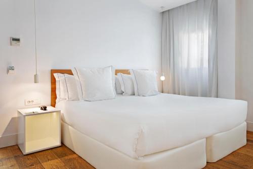 a white bedroom with a large bed with white pillows at One Shot Prado in Madrid