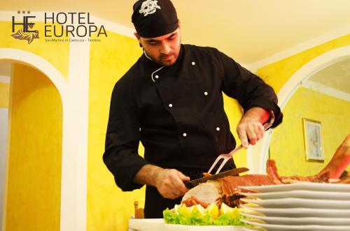 a man cutting a cake with a knife at Hotel Europa in San Martino di Castrozza