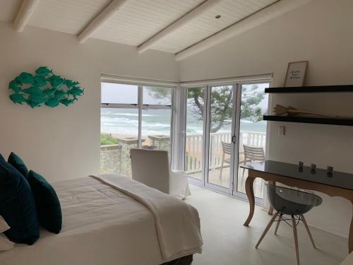 a bedroom with a bed and a desk with a view of the ocean at The Beach House - Glentana in Glentana