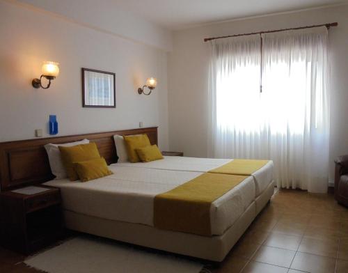 a bedroom with a bed with yellow pillows and a window at Boutique Hotel Marina S. Roque in Lagos
