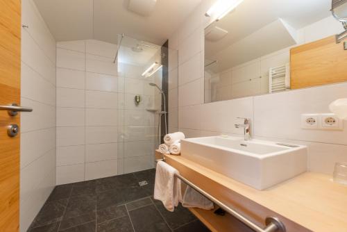 a white bathroom with a sink and a shower at Hotel Lindenhof in Ramsau am Dachstein