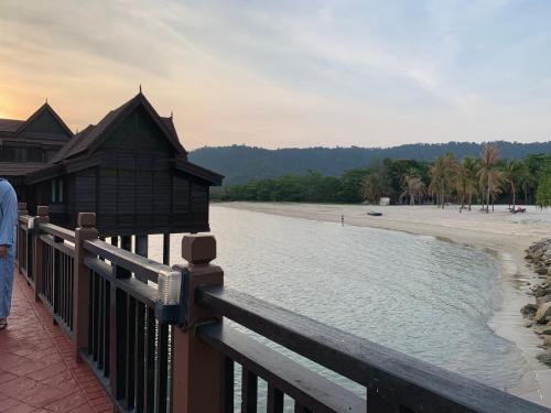 a person standing on a fence next to a beach at Langkawi Lagoon Resort Water Chalet in Pantai Cenang