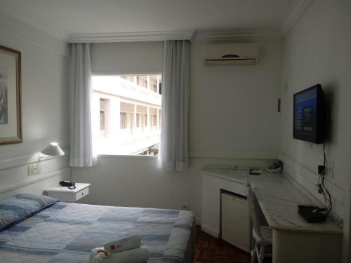 a bedroom with a bed and a desk and a window at Hotel Bruggemann in Florianópolis