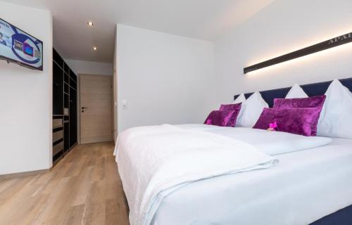 a bedroom with a large white bed with purple pillows at ImPuls | aparts in Schladming