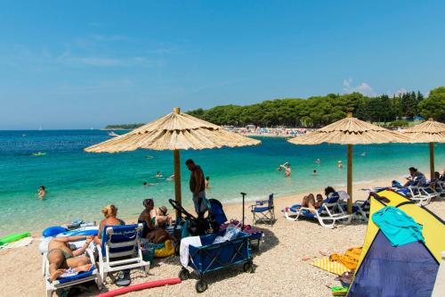 a group of people sitting on a beach with umbrellas at Apartments Danica in Primošten