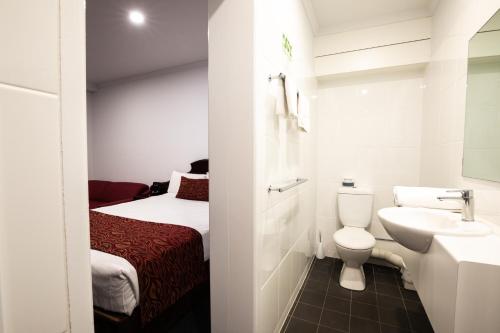 a bathroom with a sink and a toilet and a bed at Hotel Settlers in Biloela