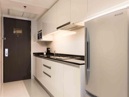 a kitchen with white cabinets and a refrigerator at Maitria Hotel Sukhumvit 18 Bangkok – A Chatrium Collection in Bangkok