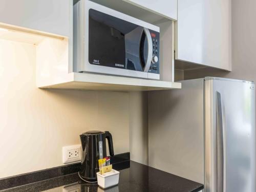 a microwave above a kitchen counter with a refrigerator at Maitria Hotel Sukhumvit 18 Bangkok – A Chatrium Collection in Bangkok