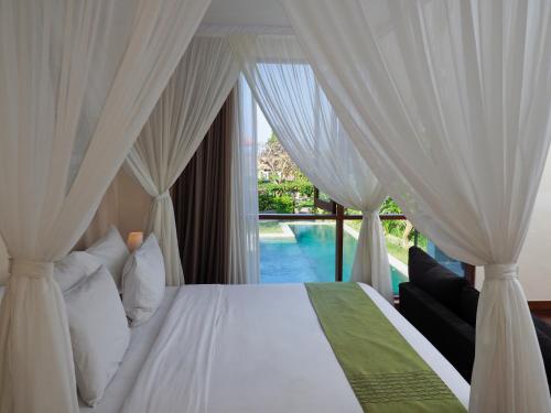 a bedroom with a bed with white curtains and a pool at The Samata by LifestyleRetreats in Sanur
