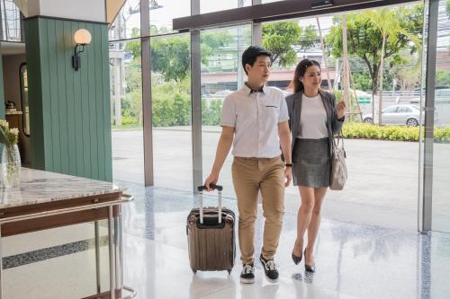 a man and a woman walking with a suitcase at Justice Hotel in Bangkok