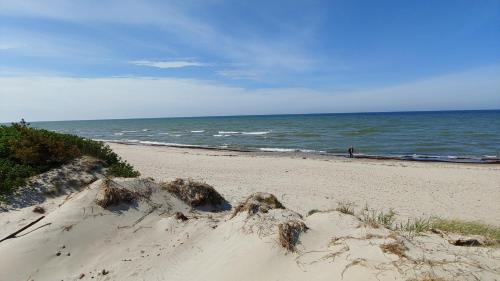 a sandy beach with a person walking on the ocean at Smiltinas in Nidden